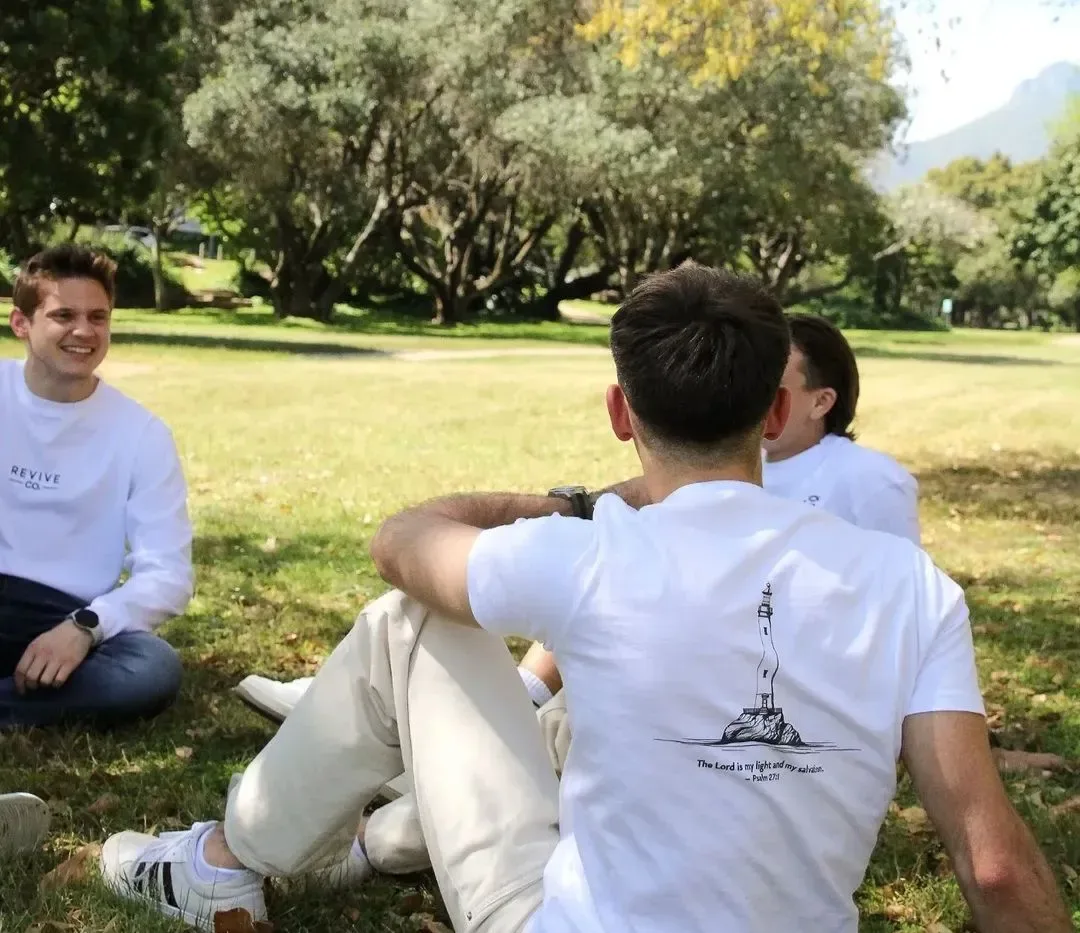 Friends sitting on the grass, one wearing The Light Tee