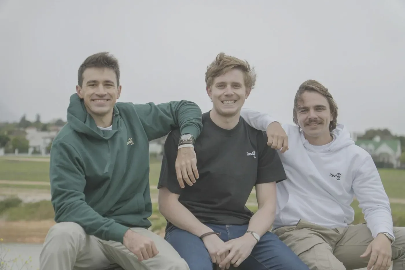 Three friends in Revive Co. hoodies and a tee, smiling outdoors