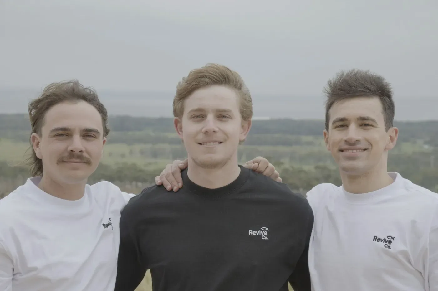 Three friends with arms around each other overlooking green fields